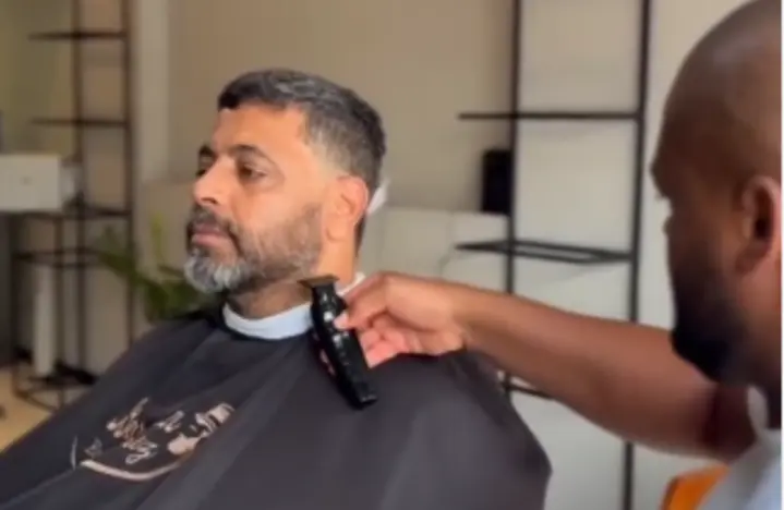 Barbeiro fazendo o acabamento da barba de um cliente com máquina profissional